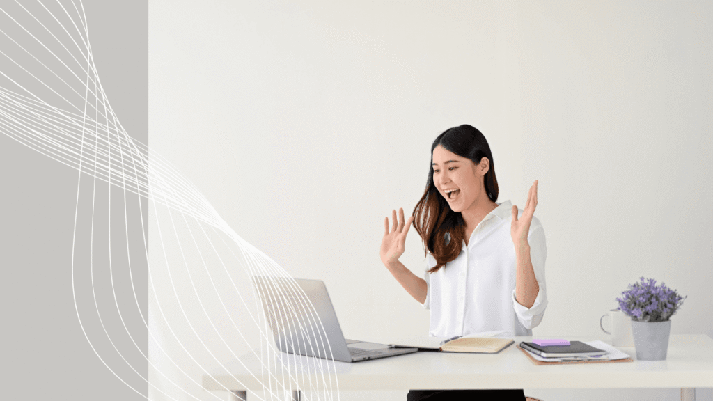 Mulher jovem comemorando com alegria ao ver resultados positivos no notebook, sentada à mesa em um ambiente claro e moderno com plantas e cadernos.